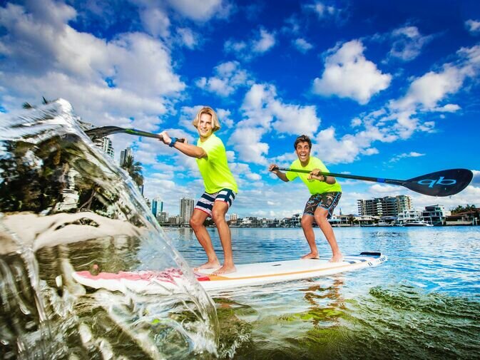 Smiling teens paddleboarding on clear Broadwater with high-rise views in the background — showcasing one of the best things to do in Gold Coast for fun, family-friendly water adventures.